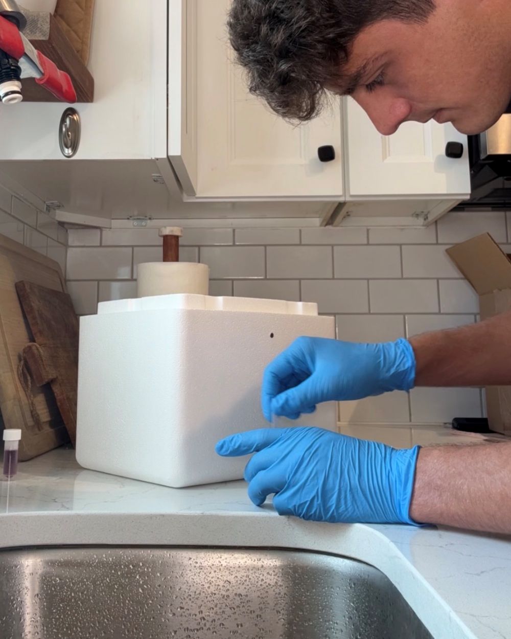 Nate Rush in nitrile gloves at a customer's kitchen sink, packing the insulated shipping cooler after drawing the sample.