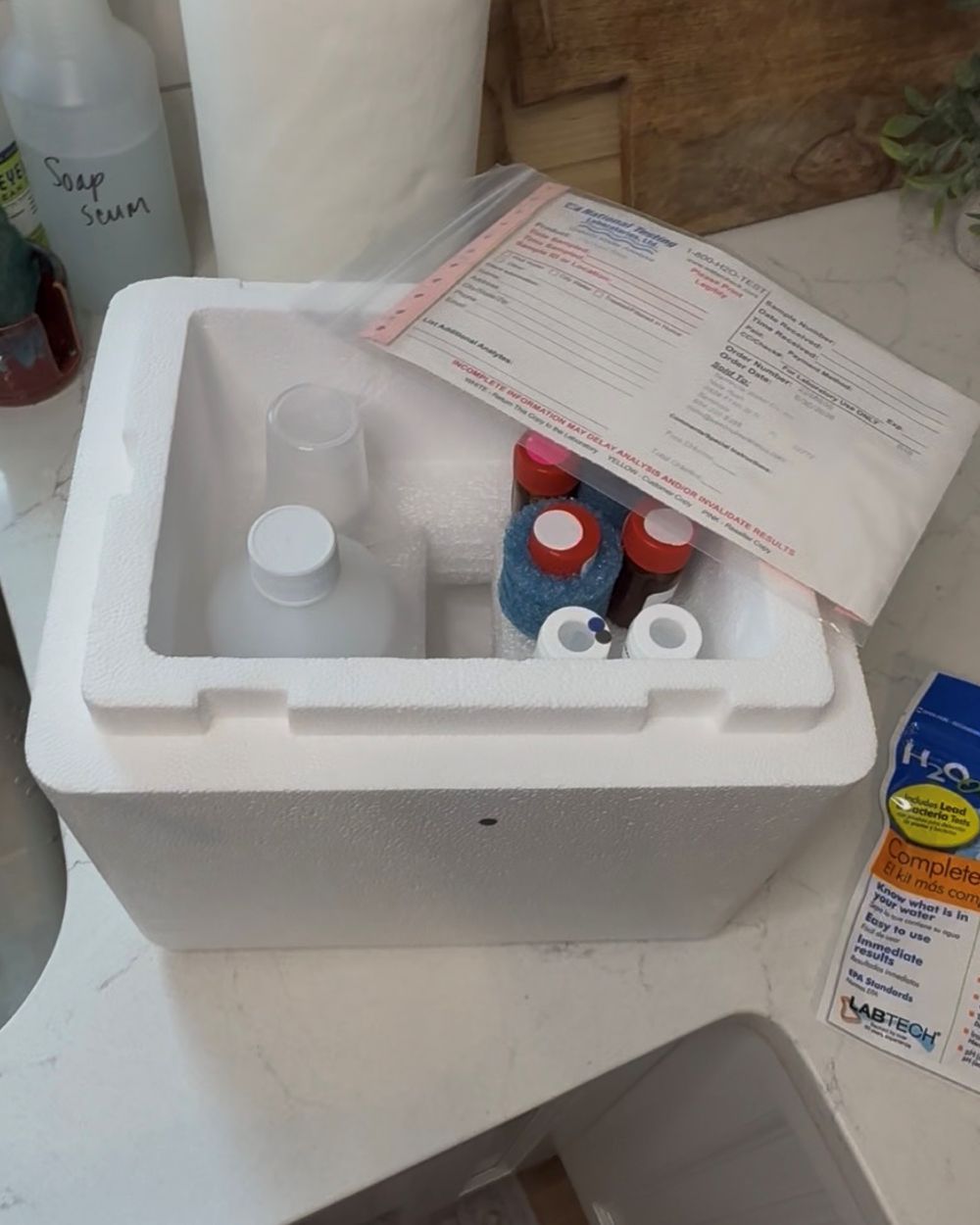 The opened National Testing Laboratories shipping kit on a counter: sample bottles, sealed vials and the chain-of-custody form.